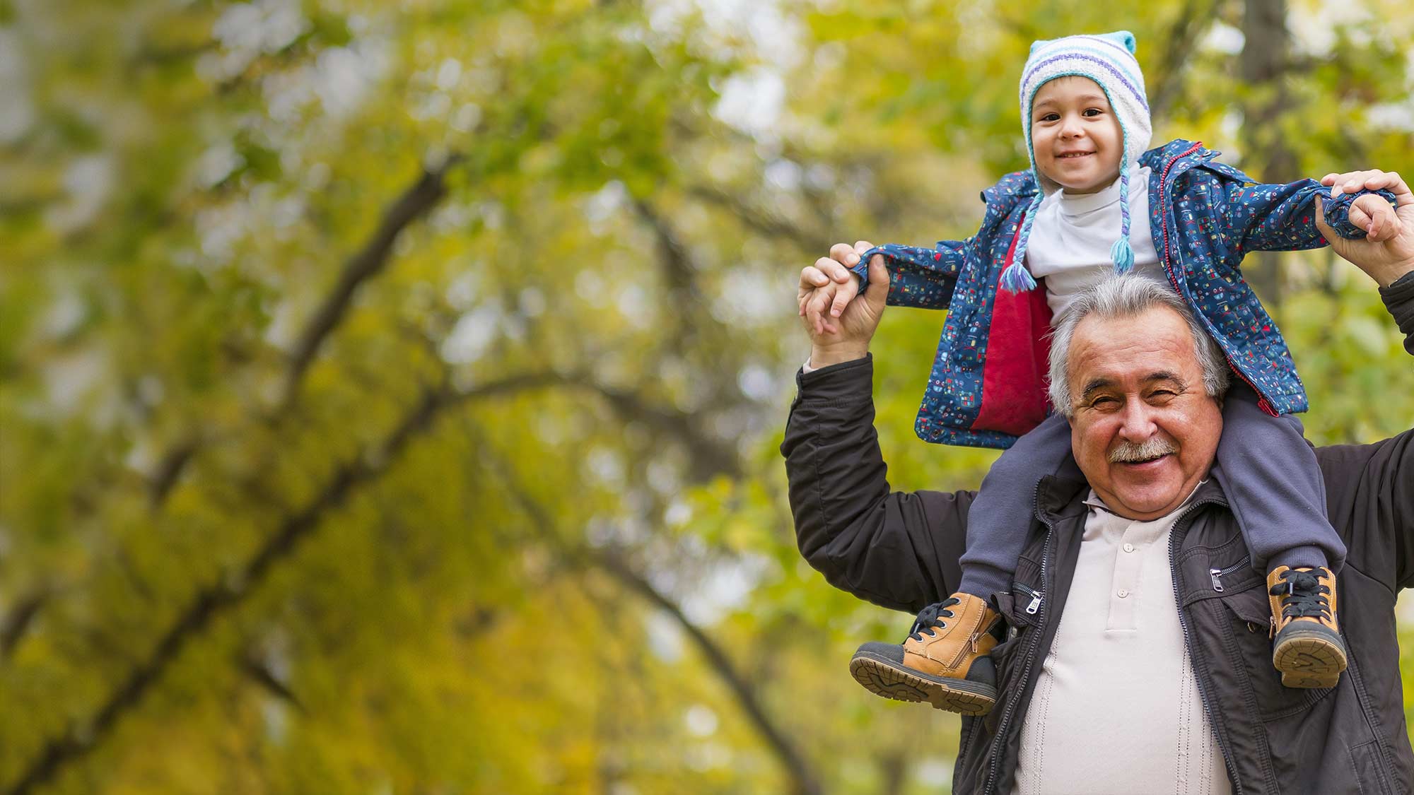 Older man with grandchild in jacket and hat on his shoulders